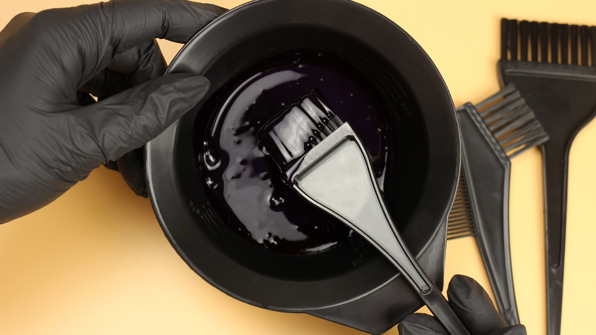 Bigen hair color mixing in black bowl with applicator brush and gloves on yellow background
