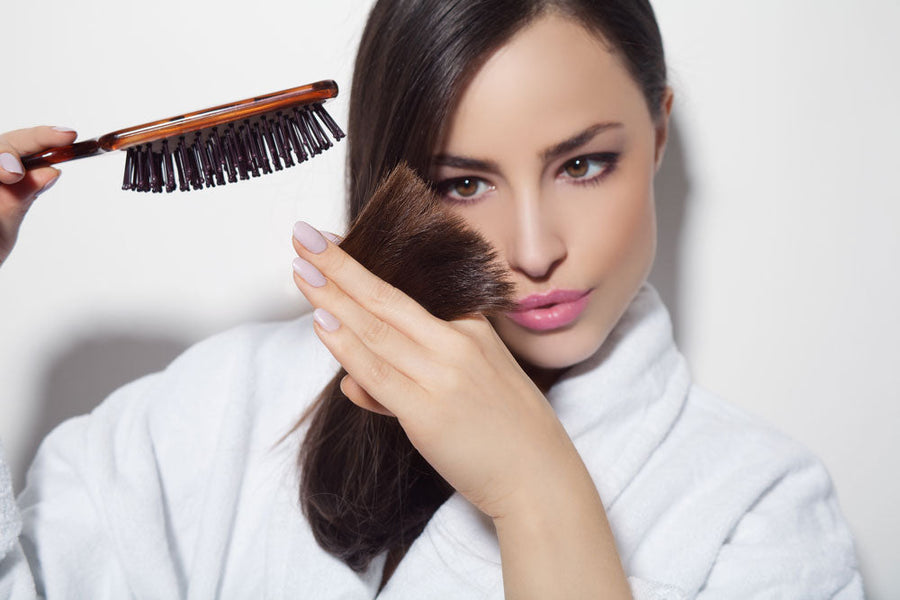 Woman examining split ends in hair, holding Bigen hairbrush, hair care focus